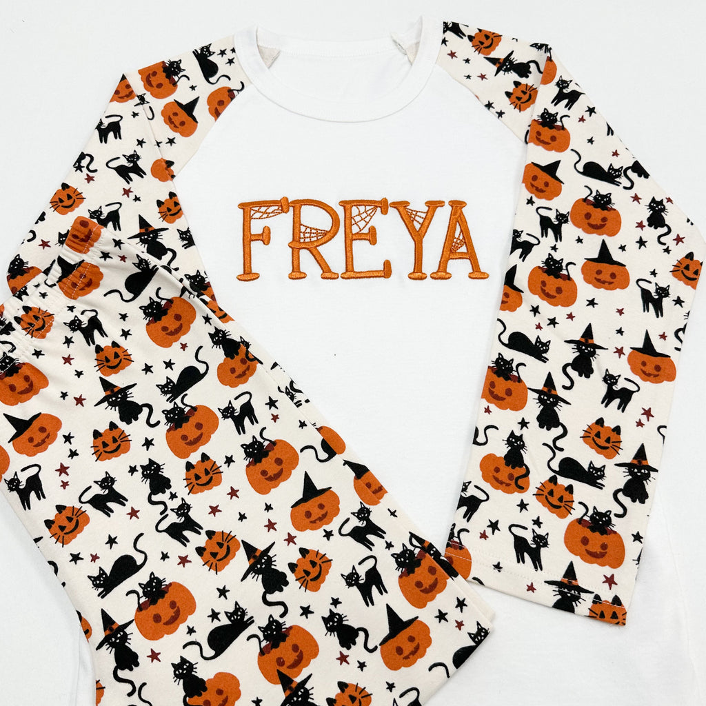 Halloween-themed shirt with pumpkins, cats, and stars on a white background