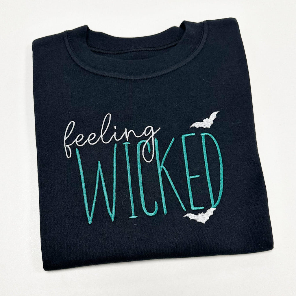 Folded black sweatshirt with 'feeling WICKED' text and bats on a white background